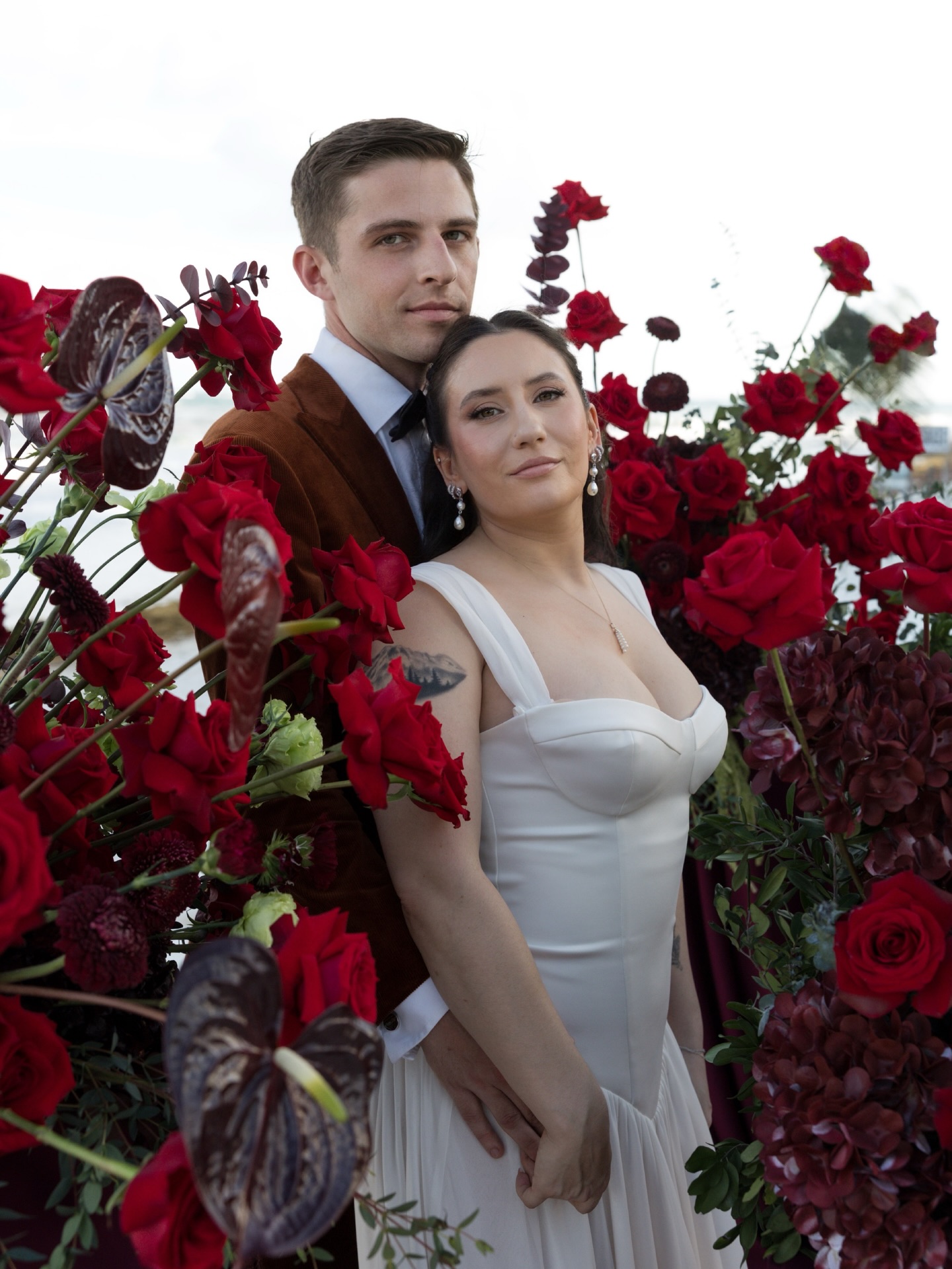 Couple surrounded by red floral arrangements.